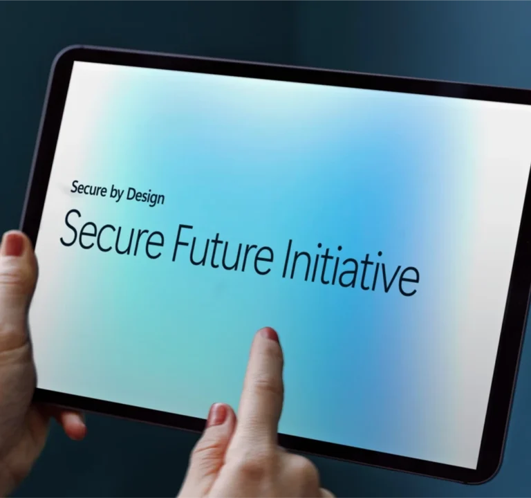 Two hands holding a table device displaying the words Secure By Design, Secure Future Initiative
